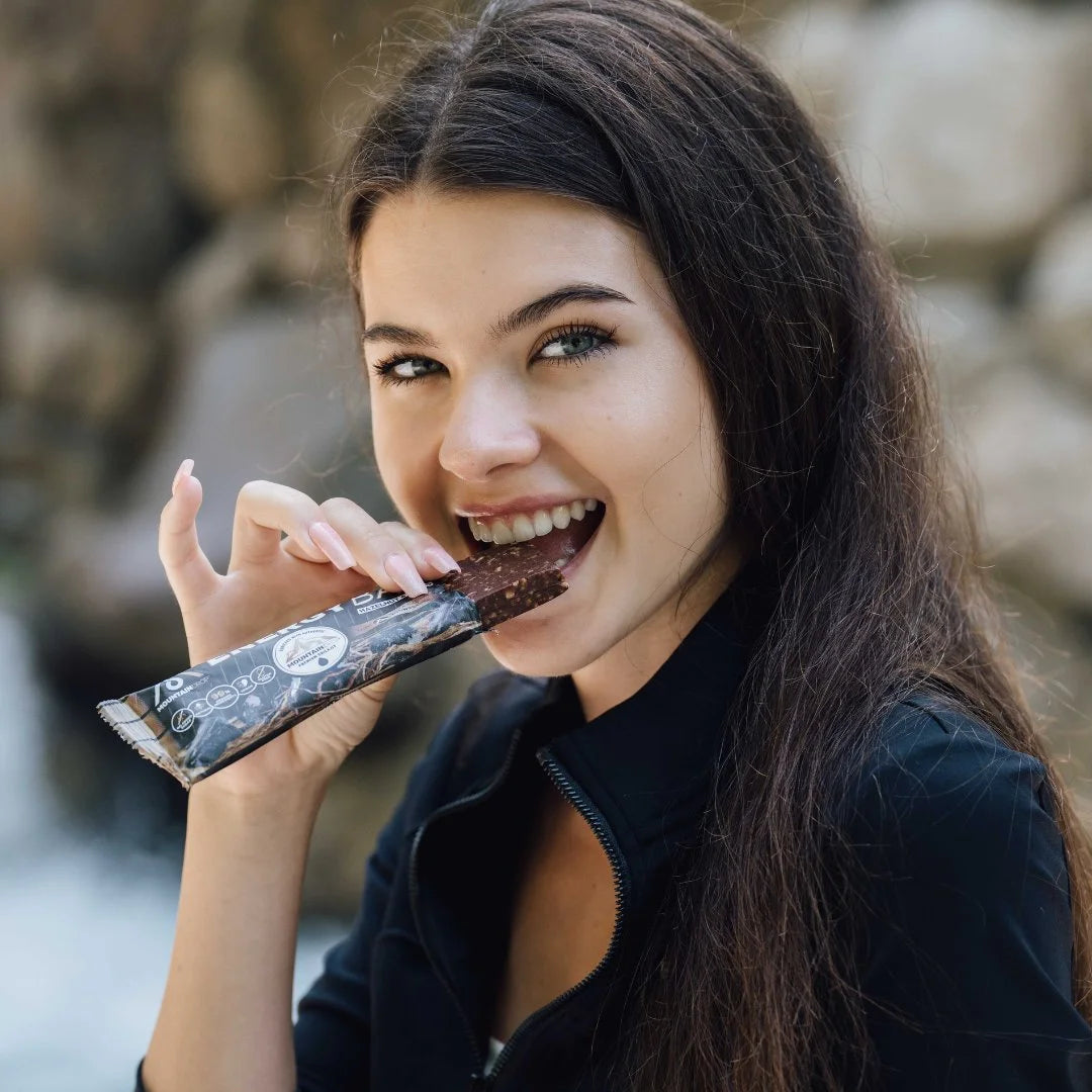 Nainen nauttii Mountaindrop Energiapatukkaa ulkona – terveellinen ja energisoiva välipala jokaiseen päivään.